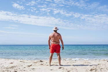 Übergewichtiger Mann mit Hut schaut an einem sonnigen Tag aufs Meer - JCMF02182