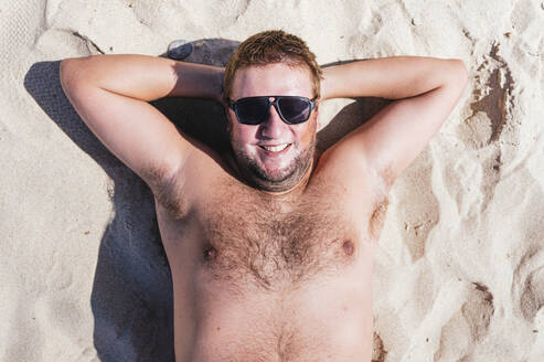 Smiling gay man relaxing on sand during sunny day - JCMF02184