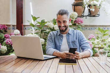 Smiling male professional talking during video call through laptop at backyard - EBBF04335