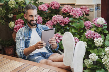 Smiling male professional using digital tablet at table in backyard - EBBF04370