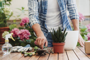 Mid adult man holding gardening fork at table in backyard - EBBF04376