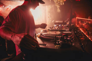 Seitenansicht eines männlichen DJs, der während eines Konzerts in einem dunklen Nachtclub Musik am Controller mischt - ADSF28206