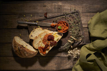 Von oben: appetitliche, frische, hausgemachte Brotscheiben mit getrockneten Tomaten und aromatischen Kräutern auf einem rustikalen Holztisch - ADSF28213