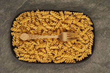 Draufsicht auf eine goldene Gabel in der Nähe von ungekochten Fusilli-Nudeln auf einem Tablett auf dem Tisch - ADSF28220