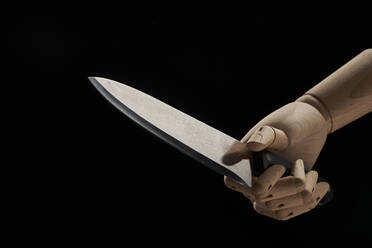 Sharp knife in wooden hand in studio on black background demonstrating concept of violence - ADSF28243