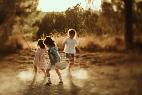 Group of carefree little girls having fun and jumping in water puddle while spending summer day together in nature - ADSF28253