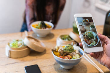 Cropped unrecognizable woman taking photo of poke dish on smartphone while spending weekend in restaurant with female friend - ADSF28264