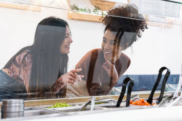 Multiracial female friends standing at counter and choosing food in restaurant while spending weekend together - ADSF28266