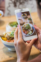 Cropped unrecognizable woman taking photo of poke dish on smartphone while spending weekend in restaurant with female friend - ADSF28270