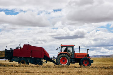 Getrocknete Heurolle und moderner Traktor auf einem landwirtschaftlichen Feld in einer Bergregion im Sommer - ADSF28313