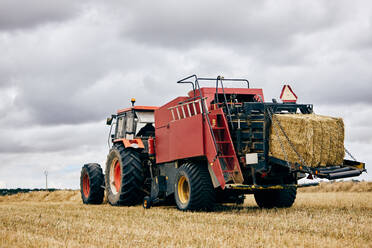Getrocknete Heurolle und moderner Traktor auf einem landwirtschaftlichen Feld in einer Bergregion im Sommer - ADSF28314
