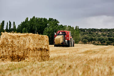 Getrocknete Heurolle und moderner Traktor auf einem landwirtschaftlichen Feld in einer Bergregion im Sommer - ADSF28315