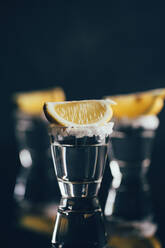 Tequila Shots mit Salz und Zitrone auf reflektierender Oberfläche vor dunklem Hintergrund - ADSF28318