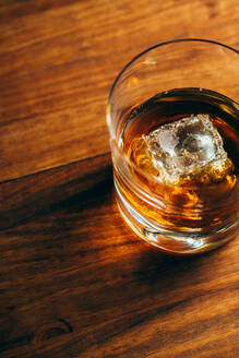 Von oben Glasbecher mit kaltem Whiskey und Eiswürfel auf Holztisch in dunklem Raum gestellt - ADSF28331