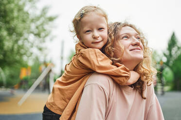 Cute little girl hugging cheerful mother in park while spending weekend together in summer - ADSF28344