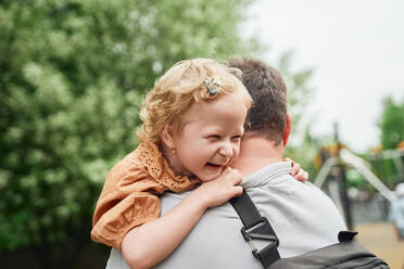 Back view father embracing cute daughter on playground in summer while looking away - ADSF28347