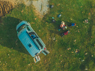 Aerial view of a group of people relaxing with a camper van in a green pad in Pyrenees, Spain. - AAEF11499