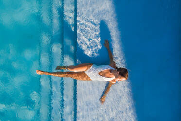 Aerial view of woman laying on the stairs of a swimming pool in a white swimsuit. - AAEF11608