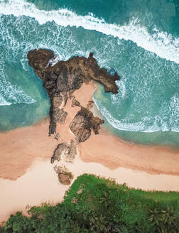 Luftaufnahme eines Mädchens, das am felsigen Privatstrand am Meer liegt, während die Wellen in Bentota, Sri Lanka, an die Oberfläche schlagen - AAEF11625