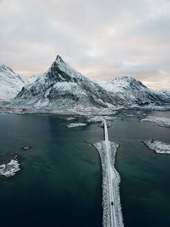 Luftaufnahme eines Autos, das über die berühmten Fredvang-Brücken und schneebedeckte Berge fährt, Lofoten-Inseln, Nordnorwegen am Polarkreis - AAEF11648