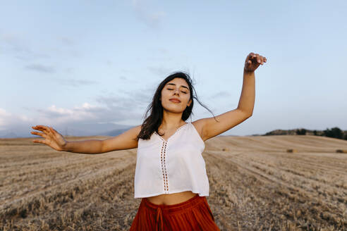 Woman with hand raised and eyes closed dancing at field - TCEF02032