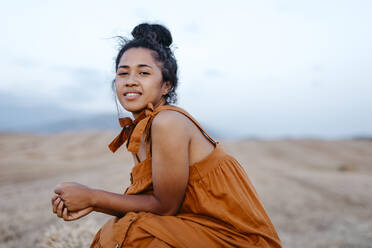 Smiling young woman sitting in farm during sunset - TCEF02043