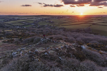 Luftaufnahme einer Person, die auf einem Felsen steht und den Sonnenuntergang in Bodmin Moor, Cornwall, Vereinigtes Königreich, betrachtet. - AAEF11855