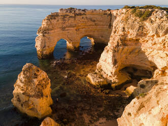 Aerial View of famous cliff formations and arches in Marinha Bay, Portugal, in the early morning right after sunrise - AAEF12089