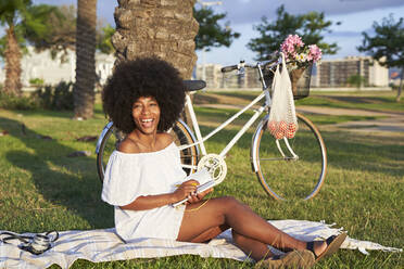 Young woman laughing while sitting with book in park - VEGF04769