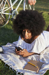 Junge Frau benutzt ein Mobiltelefon, während sie auf einer Decke liegt - VEGF04777
