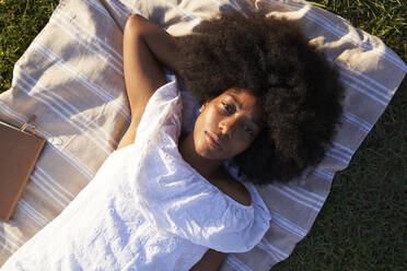 Young woman lying on blanket at public park - VEGF04783