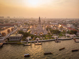 Luftaufnahme der Wat Arun Pagode entlang des Chao Phraya Flusses bei Sonnenuntergang mit einem städtischen Wohnviertel im Hintergrund, Khet Phra Nakhon Bezirk, Bangkok, Thailand. - AAEF12139