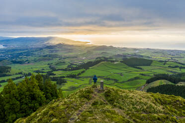 Aerial view of a hiker looking over Sao Miguel island landscape at sunset on Azores archipelagos, Portugal - AAEF12238
