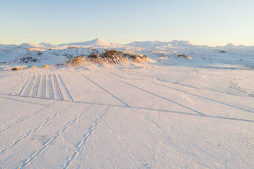 Winterliche Luftaufnahme des ersten Sonnenlichts des Tages über schneebedeckten Feldern vor Bergen, Snaefellsnes, Westisland - AAEF12361