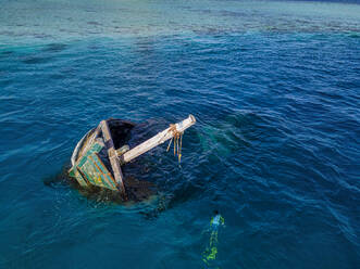 Aerial view of lone man snorkeling around sunken shipwreck - KNTF06299