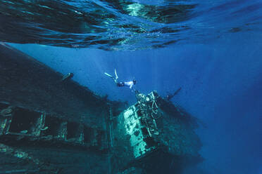 Man swimming underwater near abandoned ship in sea - KNTF06343