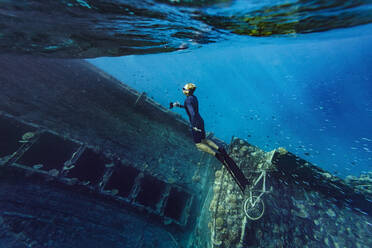 Junger Mann in Taucherflossen schwimmt an einem Schiffswrack im Meer - KNTF06345