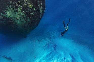 Young man swimming towards abandoned ship undersea - KNTF06346