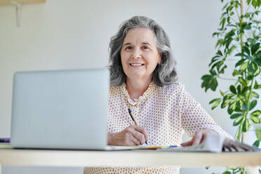 Lächelnde Geschäftsfrau sitzt mit Laptop am Schreibtisch - KIJF04061