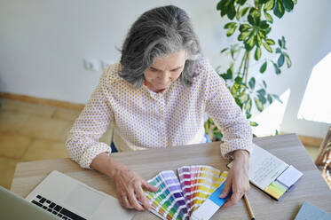 Female design professional choosing from color swatch at desk - KIJF04063