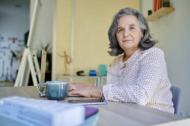 Ältere Geschäftsfrau mit Kaffeetasse und Laptop am Schreibtisch sitzend - KIJF04067