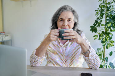 Geschäftsfrau trinkt Kaffee, während sie am Schreibtisch sitzt - KIJF04068
