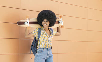 Afro-Frau hält Skateboard, während sie vor einer Wand steht - JCCMF03289