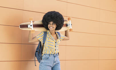 Afro woman holding skateboard while standing in front of wall - JCCMF03289