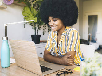 Junge Afro-Frau mit verschränkten Armen, die zu Hause auf ihren Laptop schaut - JCCMF03305