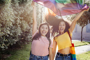 Carefree lesbian women waving rainbow flag during sunset - TCEF02049