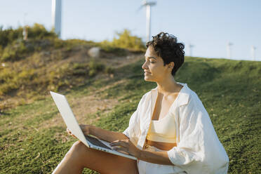 Woman holding laptop while sitting on mountain during sunny day - GMCF00169