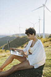 Smiling woman using laptop while sitting on mountain - GMCF00173