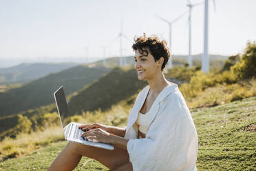 Smiling woman sitting with laptop on sunny day - GMCF00174