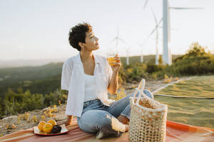 Woman holding juice glass while sitting on picnic blanket - GMCF00207